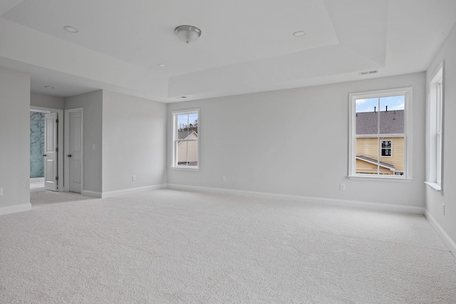 spare room featuring a tray ceiling, light colored carpet, baseboards, and visible vents