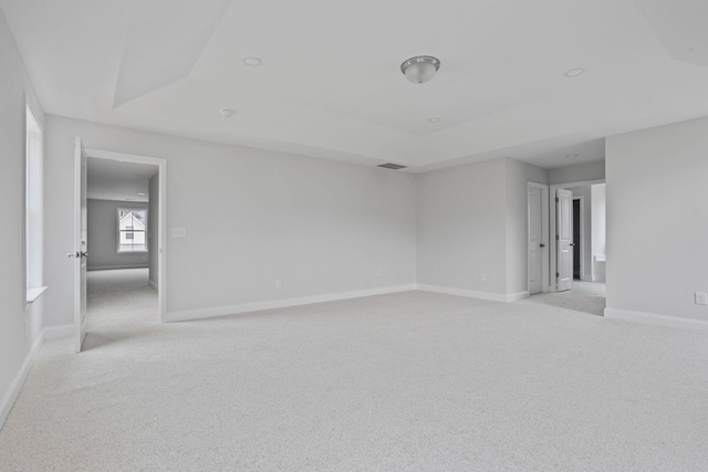 spare room with a raised ceiling, light colored carpet, baseboards, and visible vents