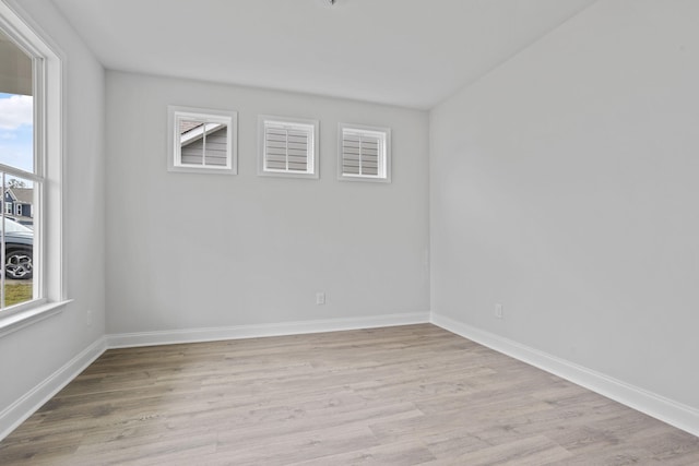 empty room with light wood-style flooring, baseboards, and a wealth of natural light