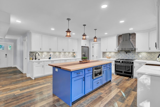 kitchen with blue cabinetry, wall chimney exhaust hood, white cabinets, and appliances with stainless steel finishes