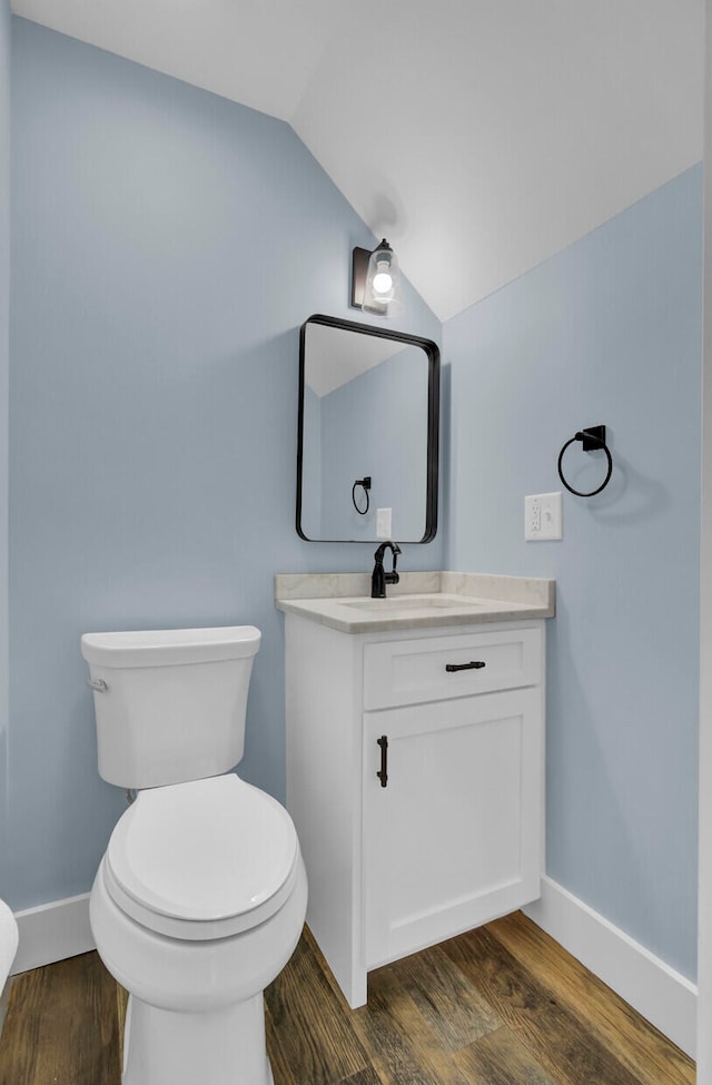 bathroom with vanity, toilet, wood-type flooring, and vaulted ceiling