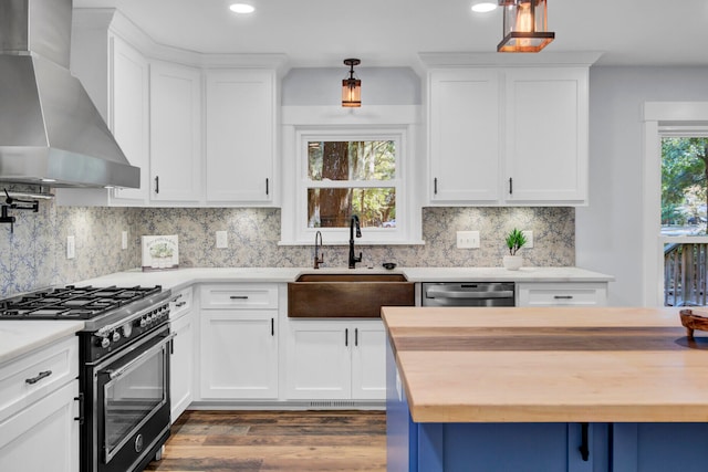 kitchen featuring gas range, wall chimney range hood, and white cabinets