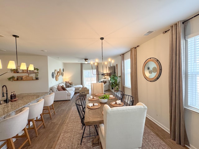 dining space with a healthy amount of sunlight, dark wood-type flooring, and ceiling fan with notable chandelier