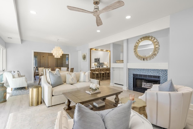 living room featuring ceiling fan with notable chandelier, a tiled fireplace, and light hardwood / wood-style floors