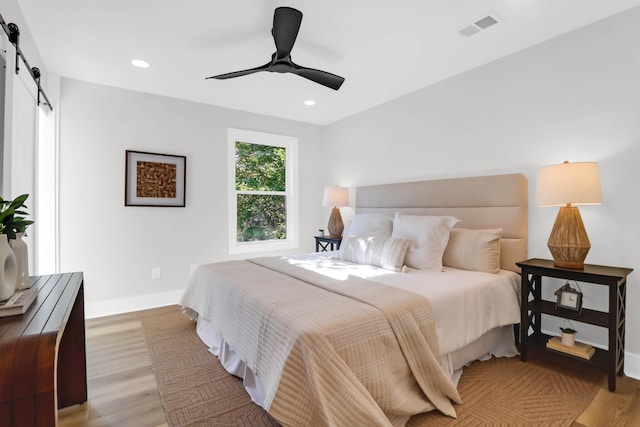 bedroom with light wood-style flooring, a barn door, baseboards, visible vents, and recessed lighting