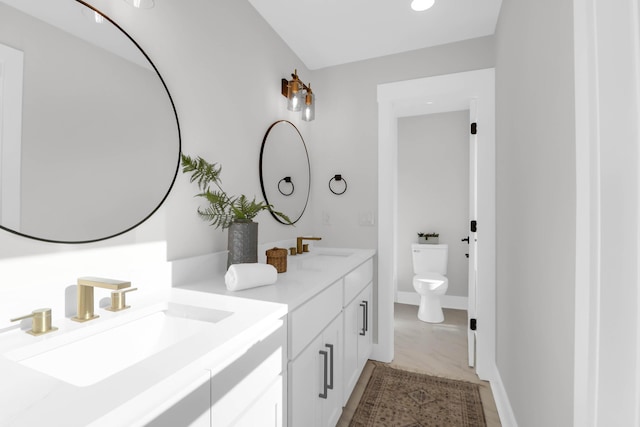 full bath with toilet, a sink, double vanity, and baseboards