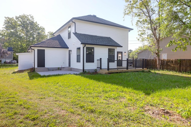 back of property featuring fence, a wooden deck, a lawn, and roof with shingles