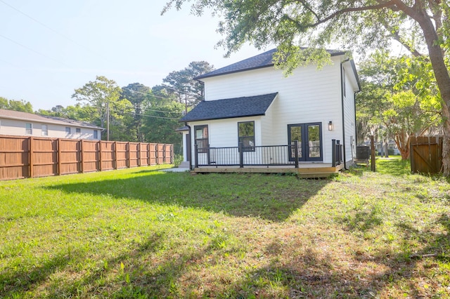 rear view of property with a deck, a shingled roof, french doors, fence, and a yard
