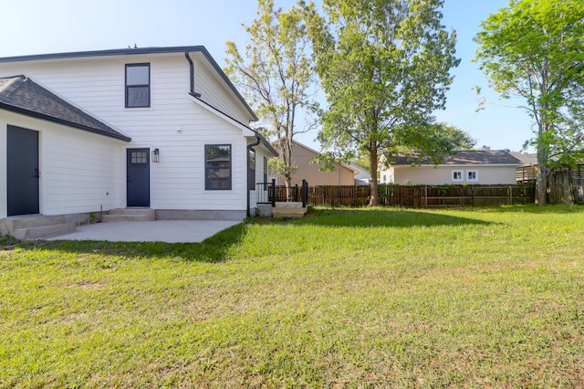 rear view of house with entry steps, a patio area, fence, and a lawn