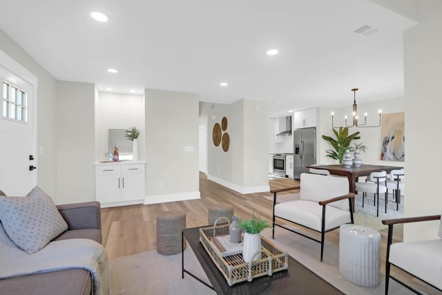 living room with baseboards, a chandelier, visible vents, and light wood-type flooring
