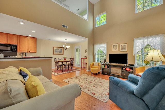 living room featuring sink, light hardwood / wood-style flooring, a towering ceiling, and a chandelier