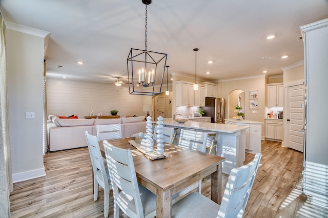 dining area with arched walkways, light wood finished floors, recessed lighting, ornamental molding, and baseboards