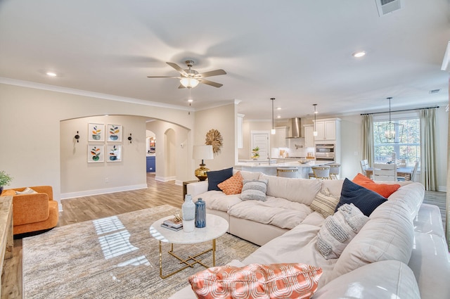 living room with light wood finished floors, visible vents, arched walkways, and crown molding