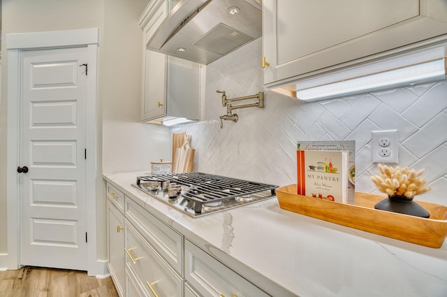 kitchen with white cabinets, range hood, stainless steel gas stovetop, and decorative backsplash