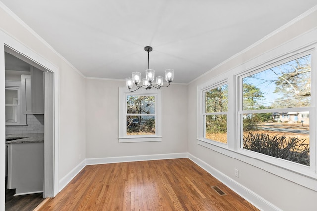 unfurnished dining area featuring a chandelier, hardwood / wood-style floors, a wealth of natural light, and ornamental molding