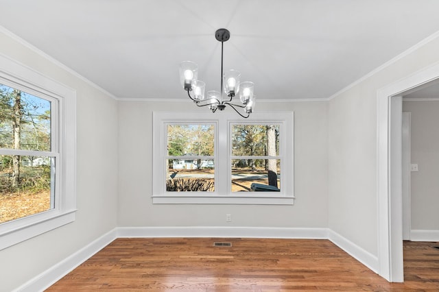 unfurnished dining area featuring hardwood / wood-style flooring, plenty of natural light, crown molding, and a notable chandelier