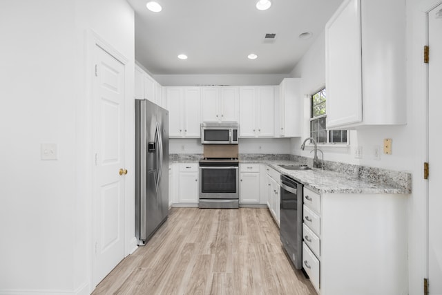 kitchen featuring sink, light stone counters, light hardwood / wood-style floors, white cabinets, and appliances with stainless steel finishes