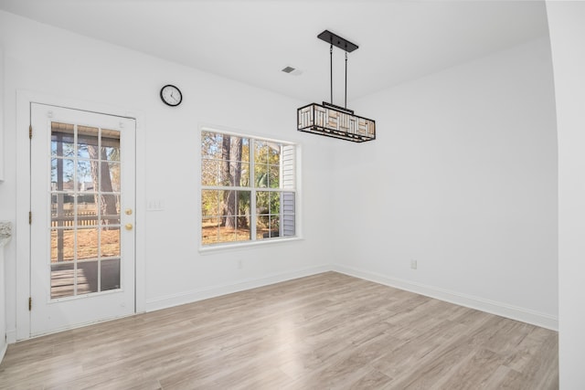 unfurnished dining area with a healthy amount of sunlight, light wood-type flooring, and a chandelier