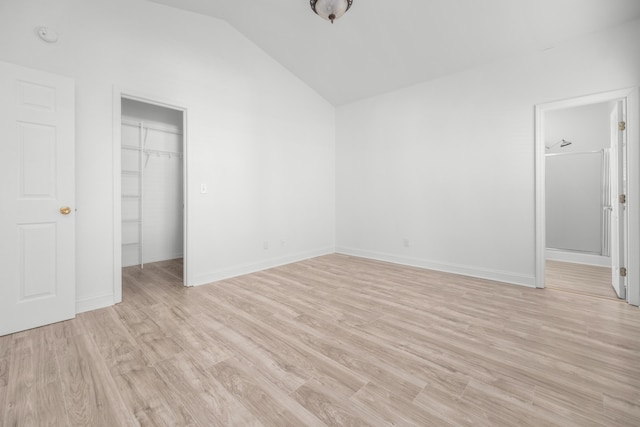 unfurnished bedroom with a walk in closet, light wood-type flooring, a closet, and vaulted ceiling