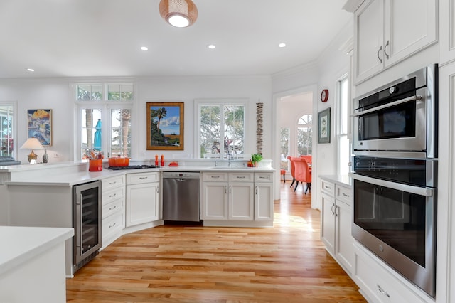 kitchen featuring white cabinets, stainless steel appliances, beverage cooler, light wood-type flooring, and ornamental molding