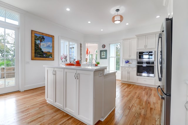 kitchen with white cabinets, appliances with stainless steel finishes, light wood-type flooring, and an island with sink