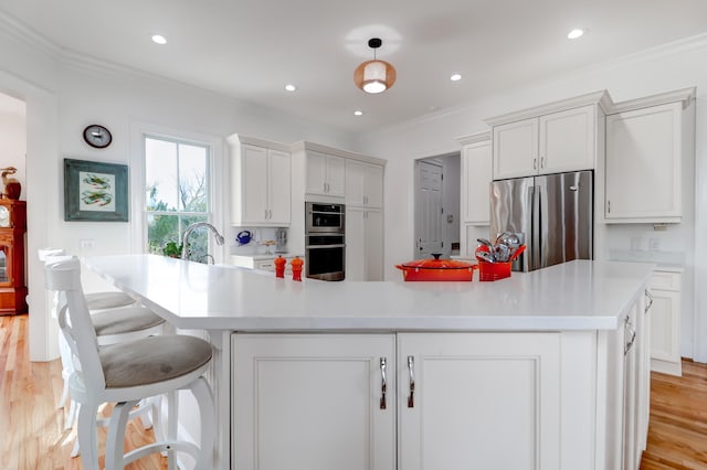 kitchen with light hardwood / wood-style floors, pendant lighting, stainless steel appliances, and an island with sink