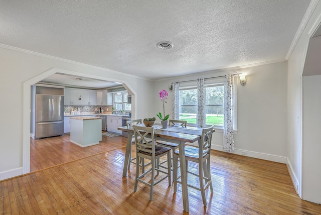 1314 Cooper Store Rd, Moncks Corner, SC 29461 - dining area featuring light wood-style floors, arched walkways, crown molding, a textured ceiling, and baseboards