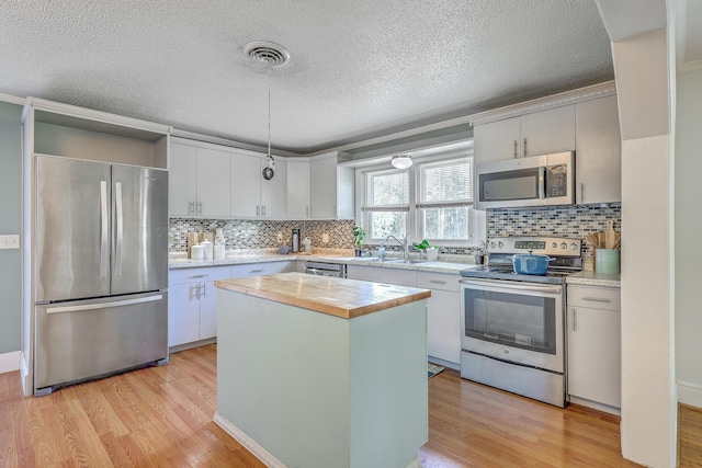 1314 Cooper Store Rd, Moncks Corner, SC 29461 - kitchen featuring appliances with stainless steel finishes, light wood-type flooring, a center island, a textured ceiling, and decorative backsplash