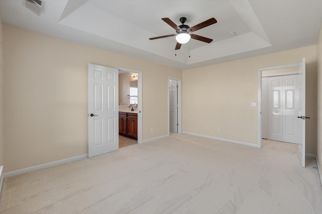 unfurnished bedroom featuring connected bathroom, light colored carpet, a sink, baseboards, and a tray ceiling