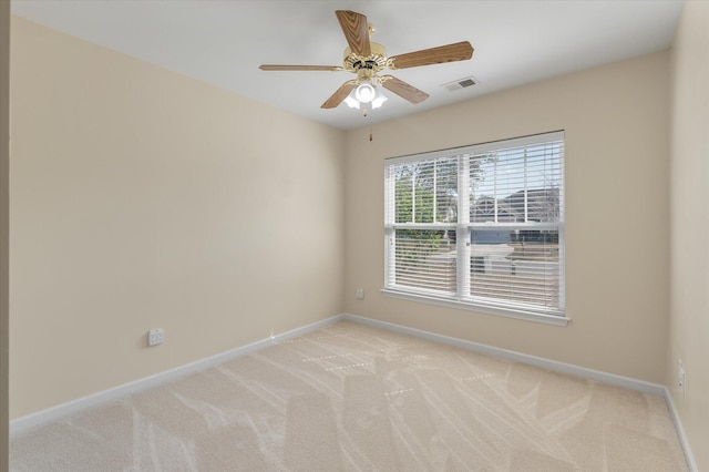 spare room with a ceiling fan, light colored carpet, visible vents, and baseboards