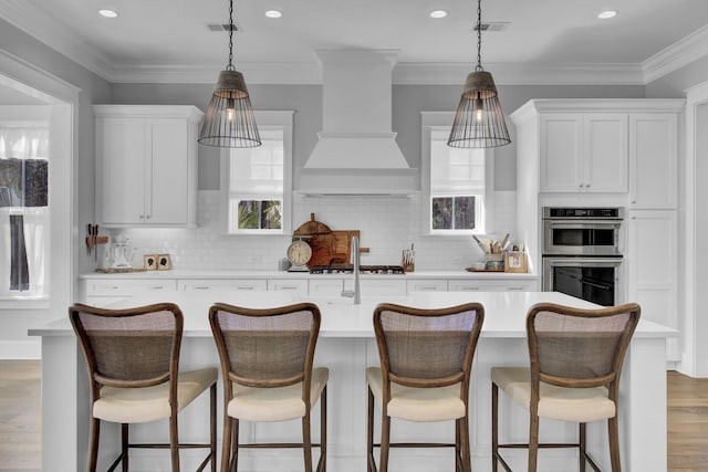 1098 Reserve Ln, Awendaw, SC 29429 - kitchen featuring custom range hood, light countertops, appliances with stainless steel finishes, a center island with sink, and light wood-style flooring