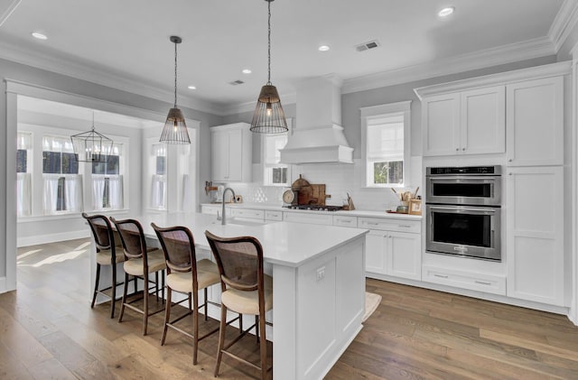 1098 Reserve Ln, Awendaw, SC 29429 - kitchen with stainless steel double oven, gas cooktop, light countertops, an island with sink, and white cabinets