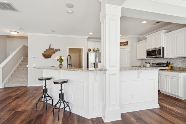 kitchen featuring stainless steel appliances, visible vents, a kitchen breakfast bar, dark wood-style floors, and decorative columns