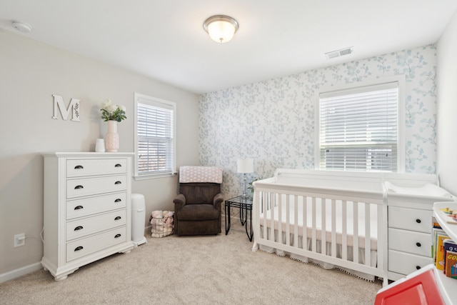 bedroom with visible vents, carpet flooring, a nursery area, baseboards, and wallpapered walls