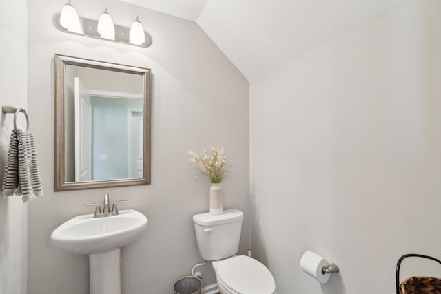 half bathroom with lofted ceiling, a sink, and toilet