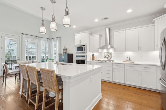 kitchen featuring appliances with stainless steel finishes, pendant lighting, an island with sink, sink, and wall chimney exhaust hood