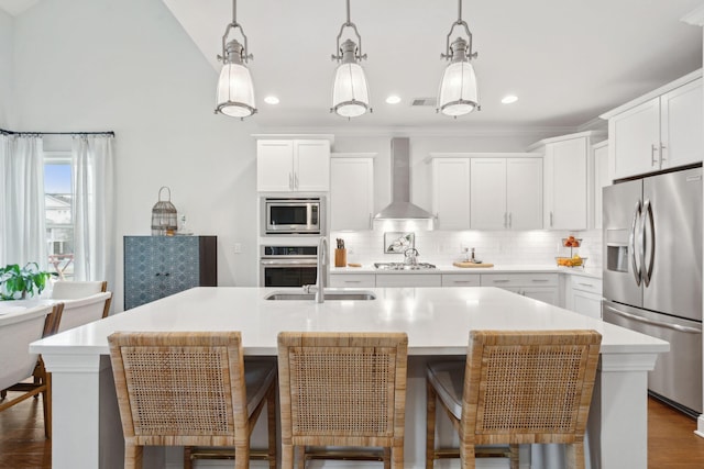 kitchen with a kitchen island with sink, hanging light fixtures, wall chimney exhaust hood, and appliances with stainless steel finishes