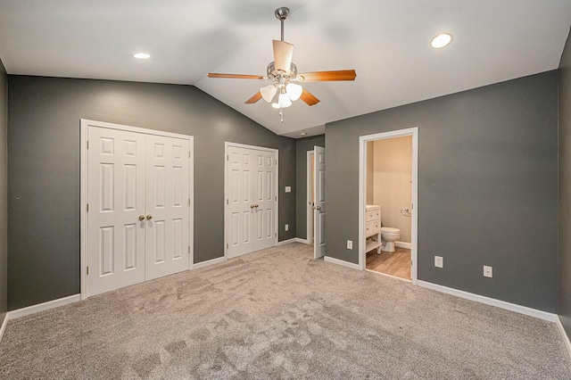 unfurnished bedroom featuring lofted ceiling, ceiling fan, multiple closets, light carpet, and ensuite bath