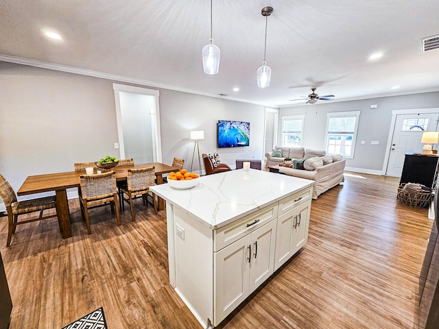 kitchen with ceiling fan, decorative light fixtures, light stone countertops, a kitchen island, and white cabinets