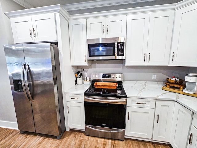 kitchen with appliances with stainless steel finishes, white cabinets, light stone countertops, ornamental molding, and light hardwood / wood-style flooring