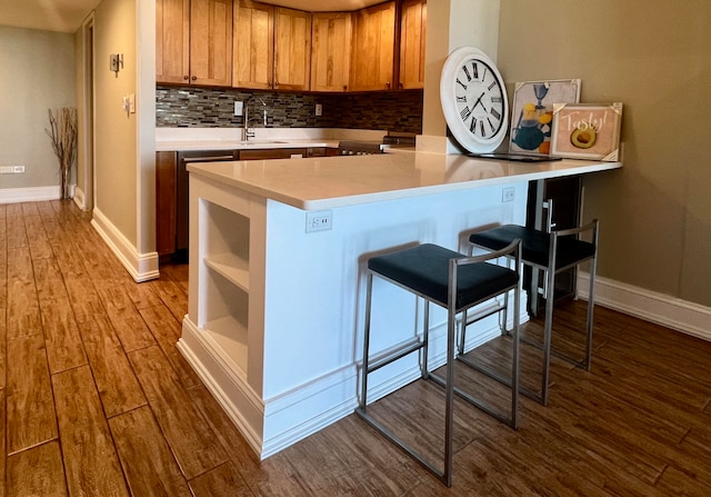 kitchen featuring light hardwood / wood-style flooring, sink, kitchen peninsula, a kitchen bar, and decorative backsplash