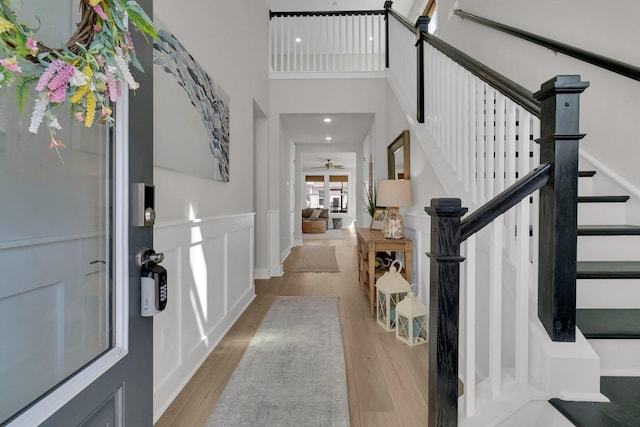 entryway featuring ceiling fan, light hardwood / wood-style floors, and a towering ceiling