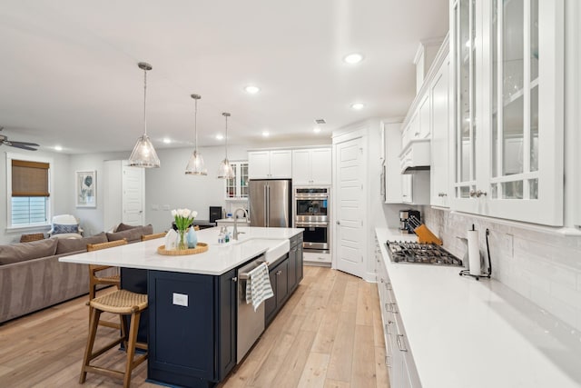 kitchen with sink, stainless steel appliances, an island with sink, decorative light fixtures, and white cabinets