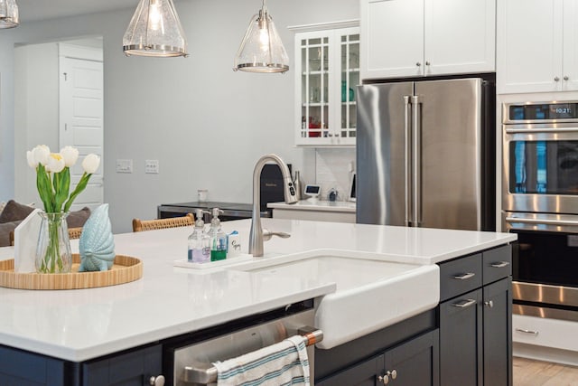 kitchen featuring white cabinetry, sink, stainless steel appliances, pendant lighting, and decorative backsplash