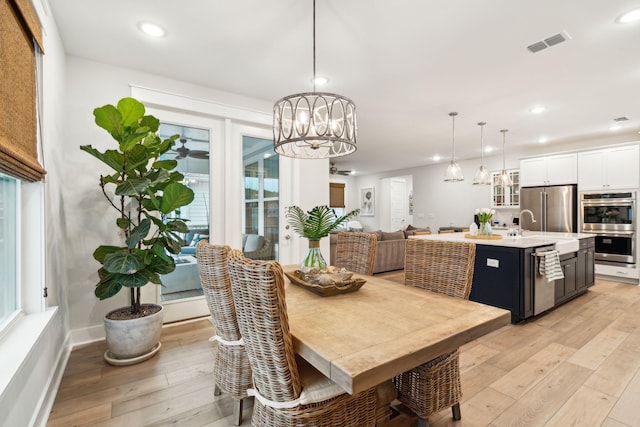 dining area with a healthy amount of sunlight, sink, light hardwood / wood-style flooring, and a chandelier