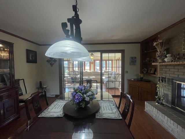 dining room featuring a fireplace, wood finished floors, built in features, and crown molding