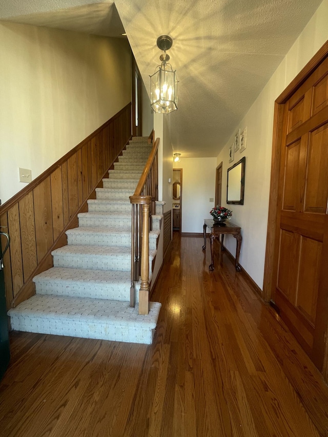 stairway with a wainscoted wall, an inviting chandelier, wood walls, a textured ceiling, and wood finished floors