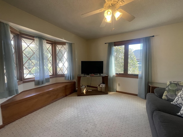 carpeted living area with ceiling fan, baseboards, and a textured ceiling