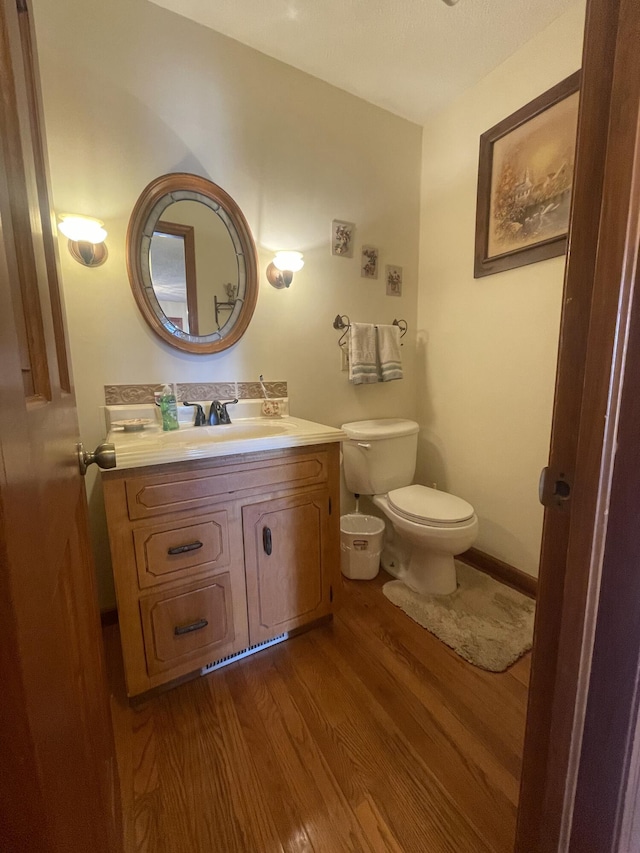 half bath with baseboards, vanity, toilet, and wood finished floors