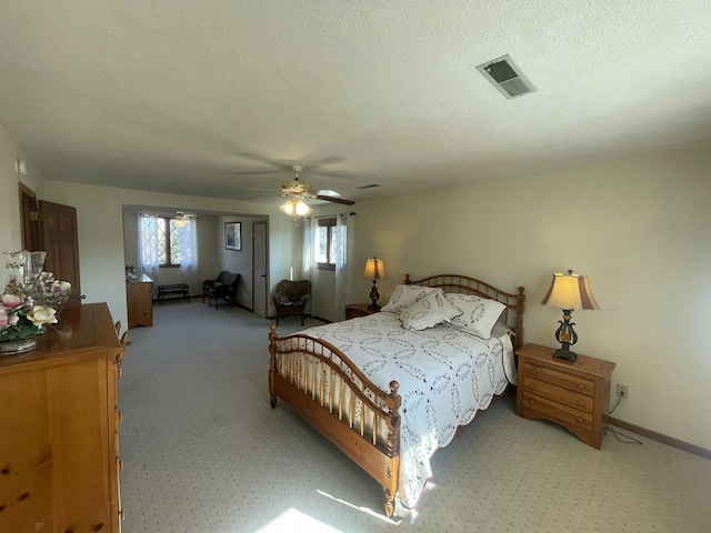 bedroom with a textured ceiling, light carpet, visible vents, baseboards, and a ceiling fan